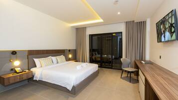 A modern hotel room with a large bed, bedside table with a lamp, a desk, and a TV.