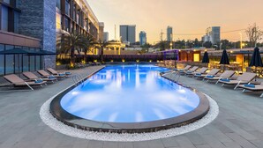 A swimming pool with lounge chairs and a cityscape in the background. - Munich Hotel (Sihanoukville)