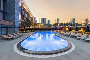 A swimming pool with lounge chairs and a cityscape in the background.
