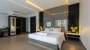 A modern hotel room with a large bed, a walk-in closet, a vanity with a mirror, and a small desk area. - Munich Hotel (Sihanoukville)