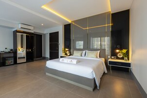 A modern hotel room with a large bed, a walk-in closet, a vanity with a mirror, and a small desk area.