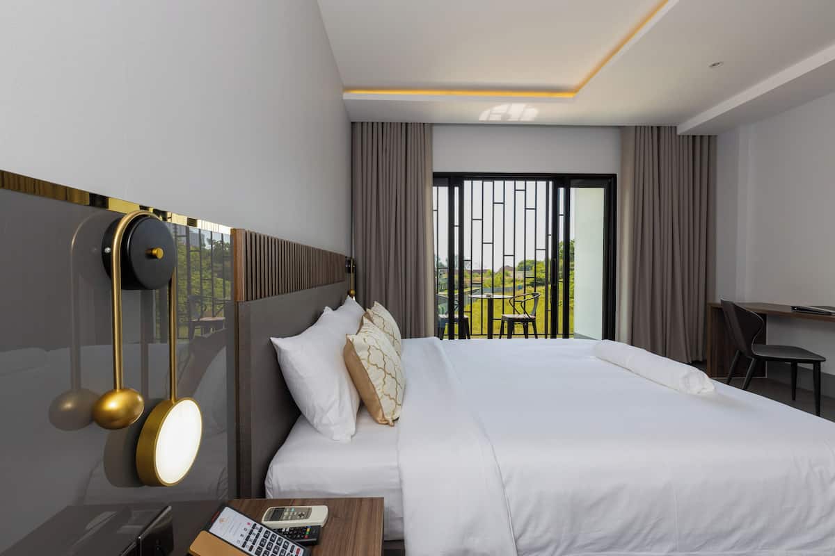A modern hotel room with a large bed, a desk, a chair, and a balcony view.
