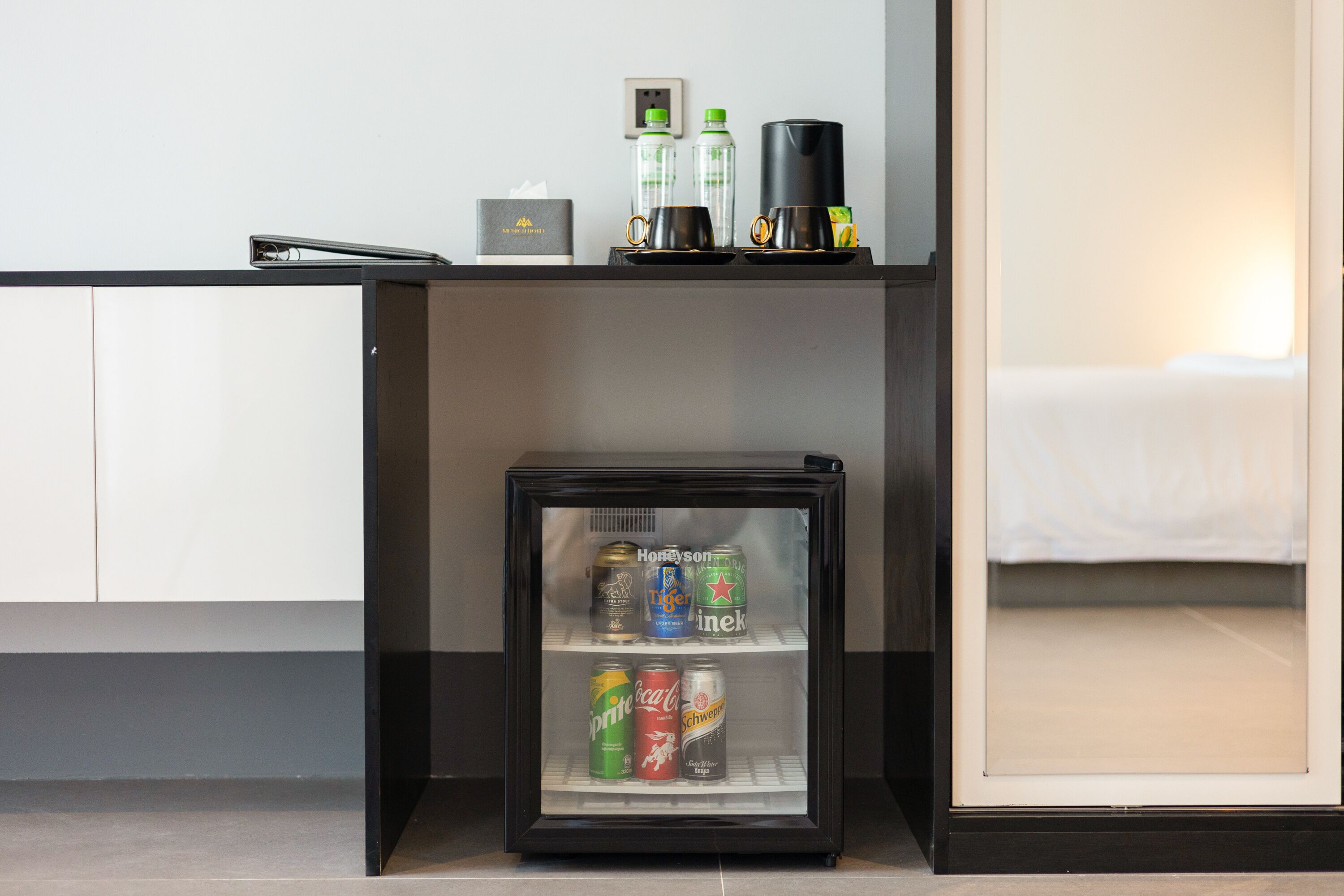 A minibar with a refrigerator containing various beverages, a coffee maker, and a tissue box.