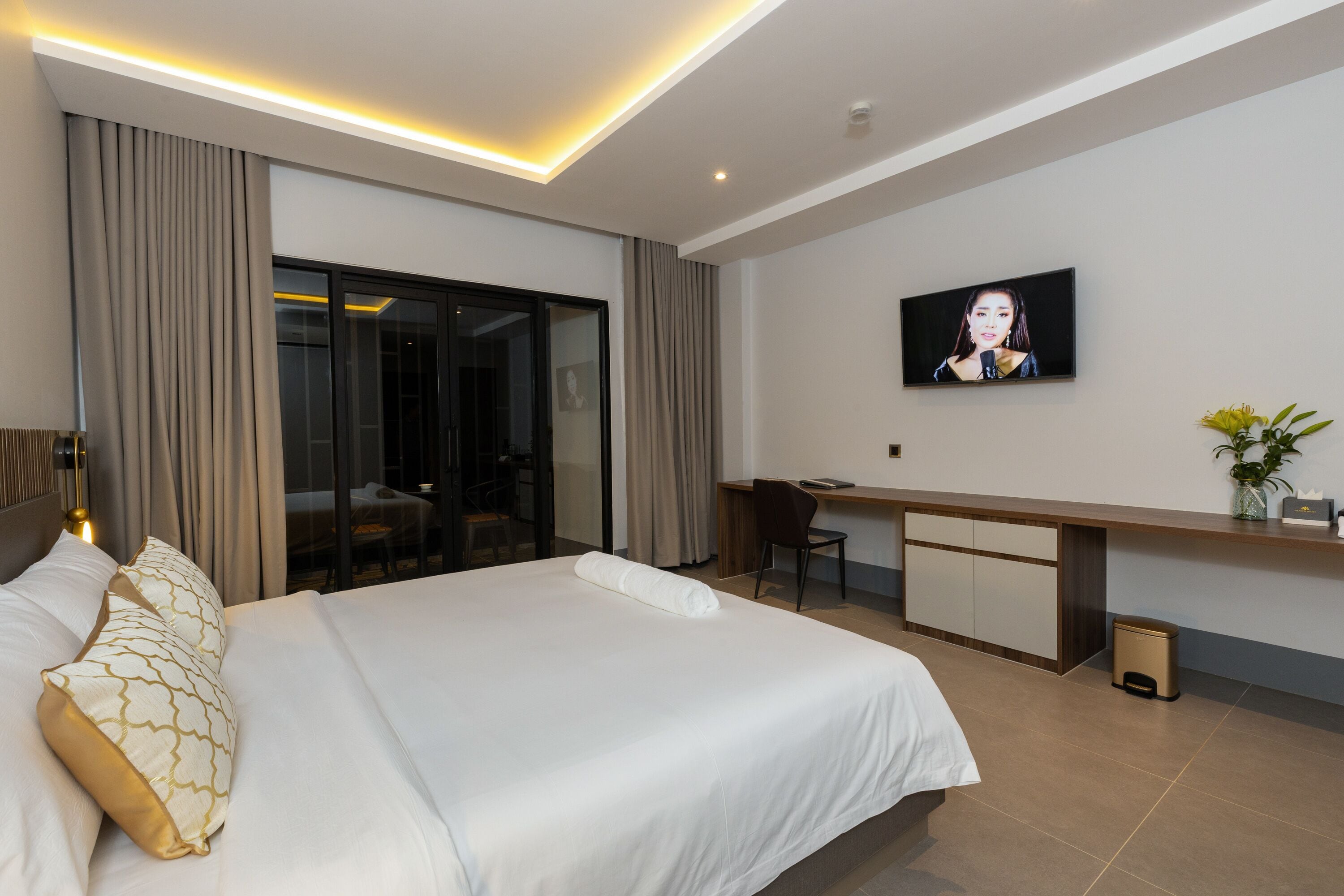 A modern hotel room with a large bed, a desk, and a television on the wall.