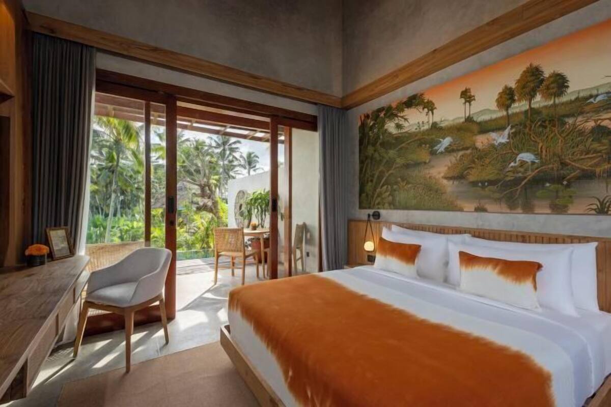 A hotel room with a large bed, a desk, and a view of a tropical landscape through the window.