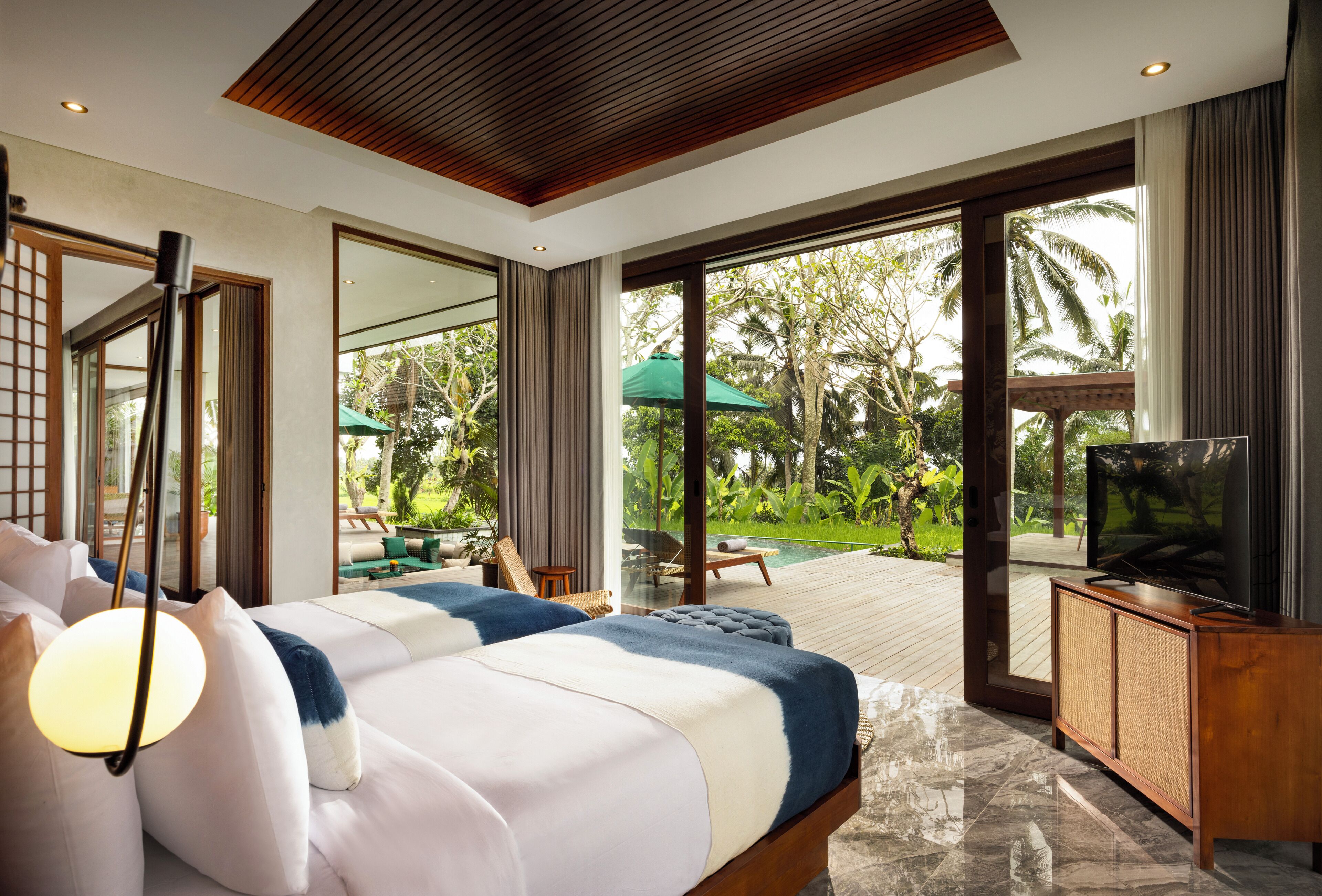A modern bedroom with a large bed, a television, and a view of a pool and garden.