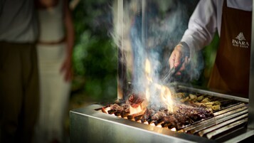 A person grilling meat on a barbecue with visible flames.