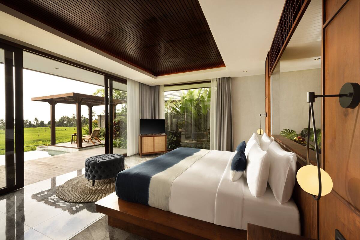 A modern bedroom with a large bed, a TV, and a view of a garden through large windows.