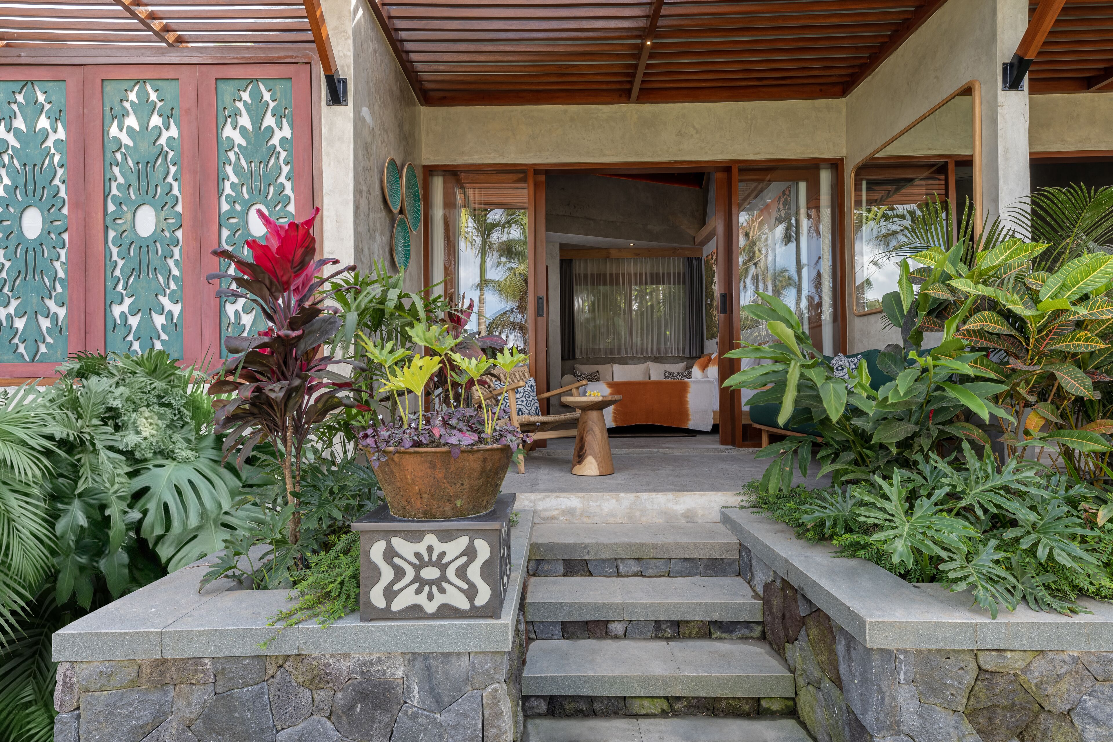 Una escalera de piedra conduce a una puerta de madera, rodeada de exuberante vegetación tropical.