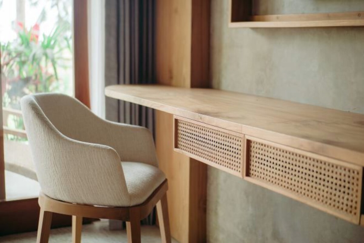A wooden desk with a perforated panel, a beige chair, and a window with natural light.