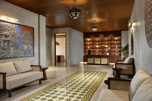 A modern interior with a sofa, chairs, a patterned rug, a wooden ceiling, and a wall with shelves.