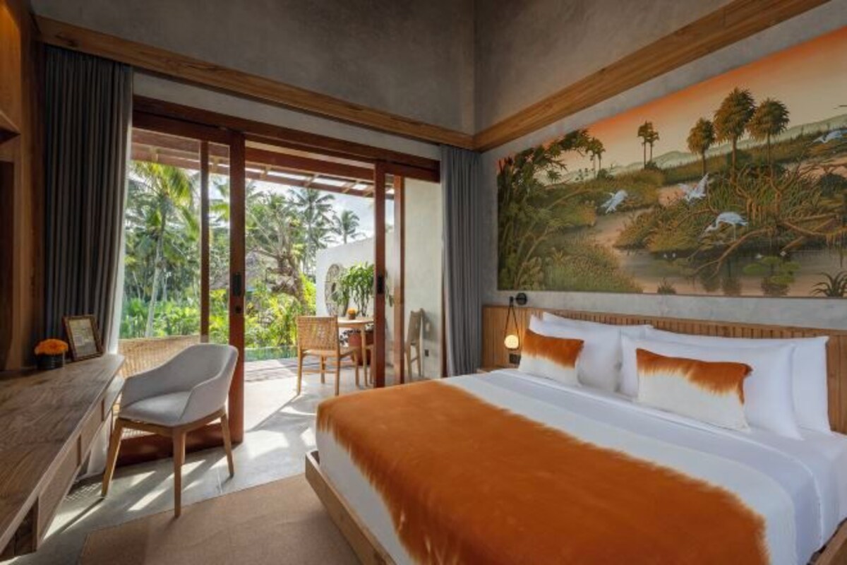 A hotel room with a large bed, a desk, and a view of a tropical landscape through the window.