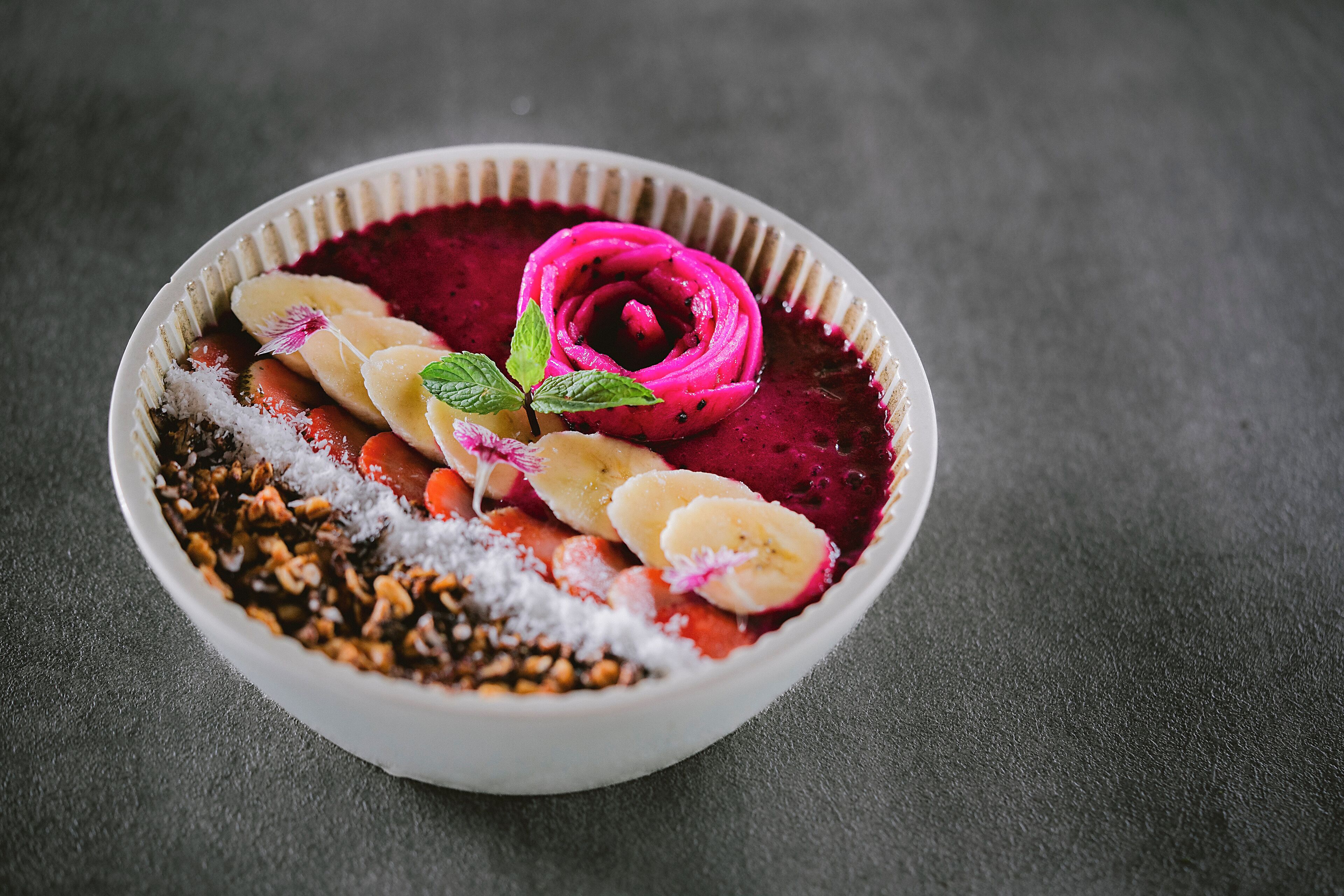 Un bol de smoothie garni de rondelles de banane, d’une feuille de menthe et d’une fleur décorative.