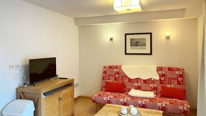 A small living room with a sofa, a TV, a wooden cabinet, and a table with two cups. - Studio Résidence LE Parc DES Airelles (LES ORRES 1800)