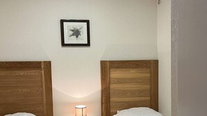 A small, clean room with two single beds, a nightstand with a lamp, and a framed picture on the wall. - Studio Résidence LE Parc DES Airelles (LES ORRES 1800)