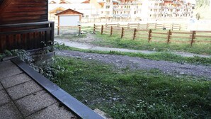 A view of a building with a wooden facade and a gravel path leading to a fenced area with greenery. - Studio Résidence LE Parc DES Airelles (LES ORRES 1800)