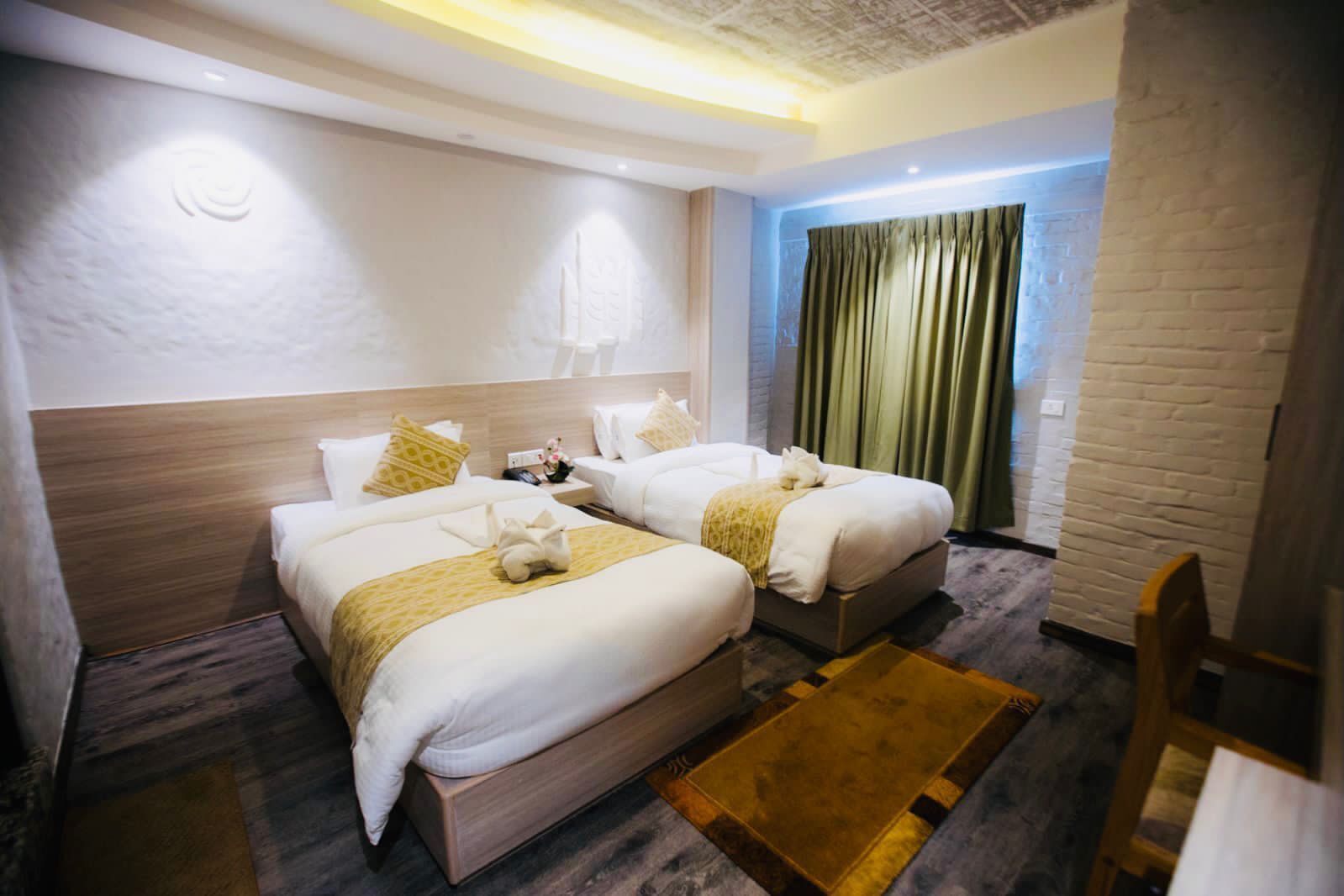Une chambre d’hôtel avec deux lits, une tête de lit en bois, une petite table de chevet, une commode, une fenêtre avec des rideaux et un mur en briques.