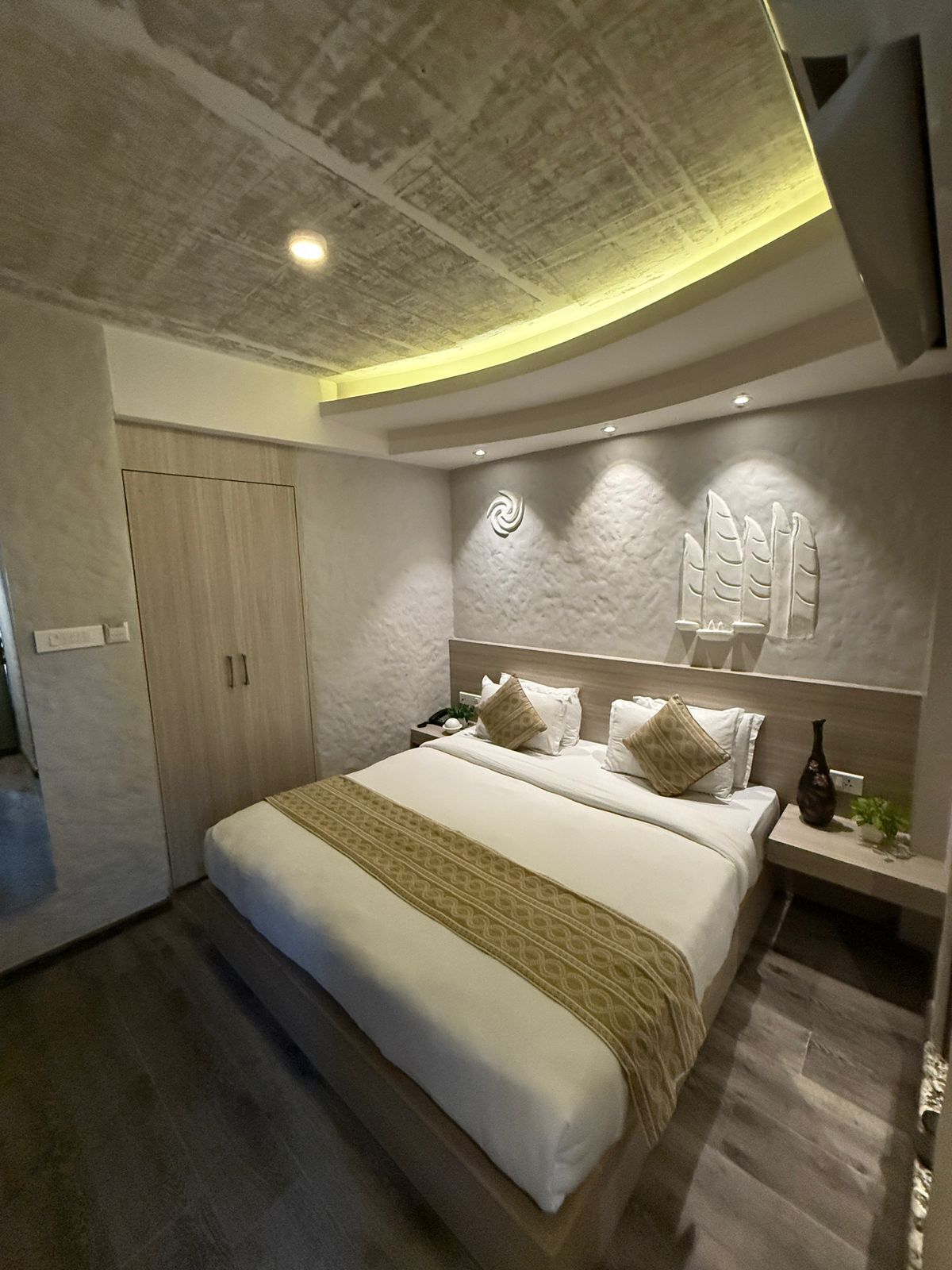 A modern bedroom with a large bed, a wardrobe, and a nightstand.