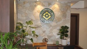 A reception desk with a stone wall backdrop, a logo, and potted plants. - Vastu Boutique Hotel (Kathmandu)