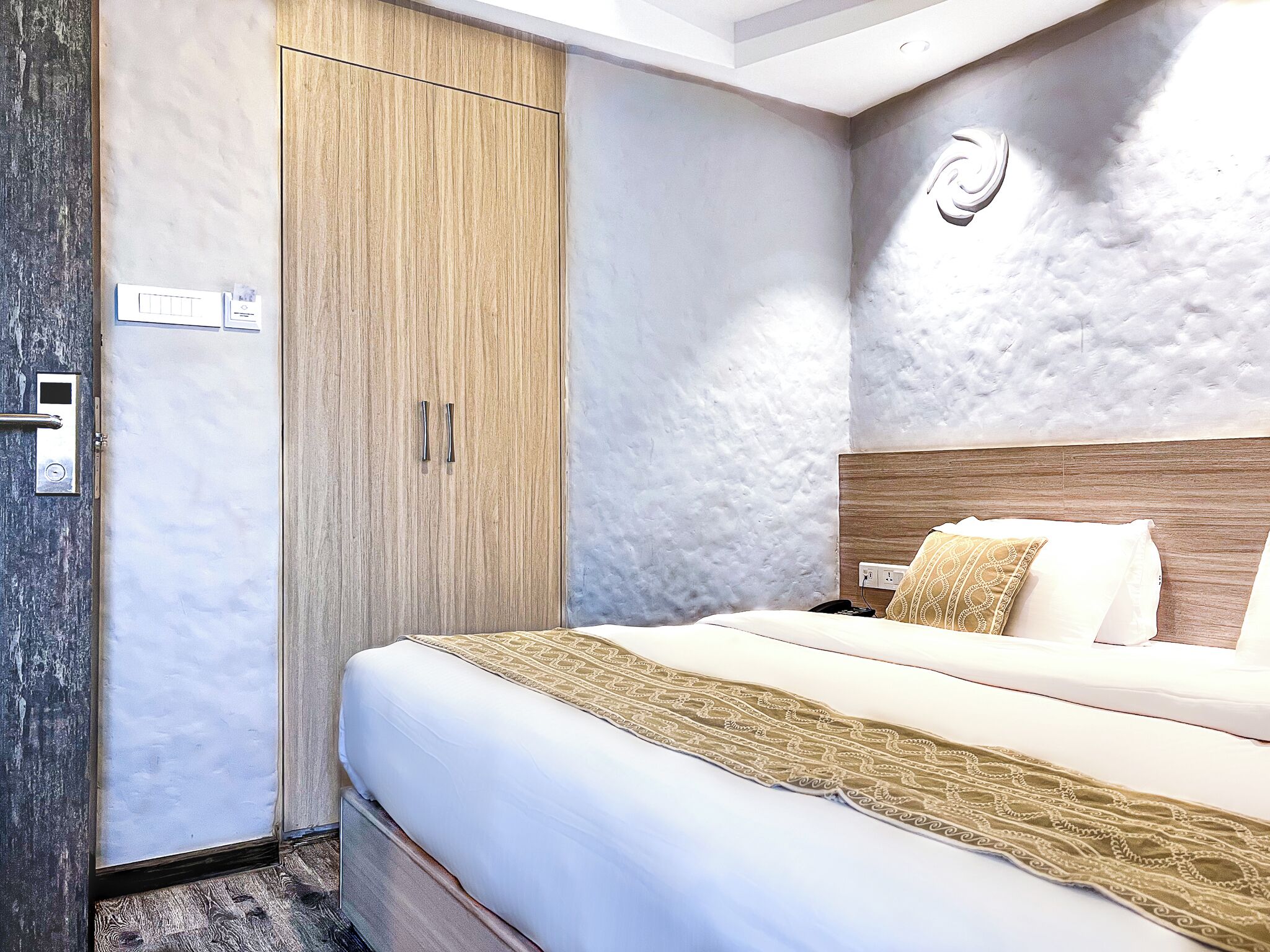 A hotel room with a bed, a wardrobe, and a wall-mounted light fixture.