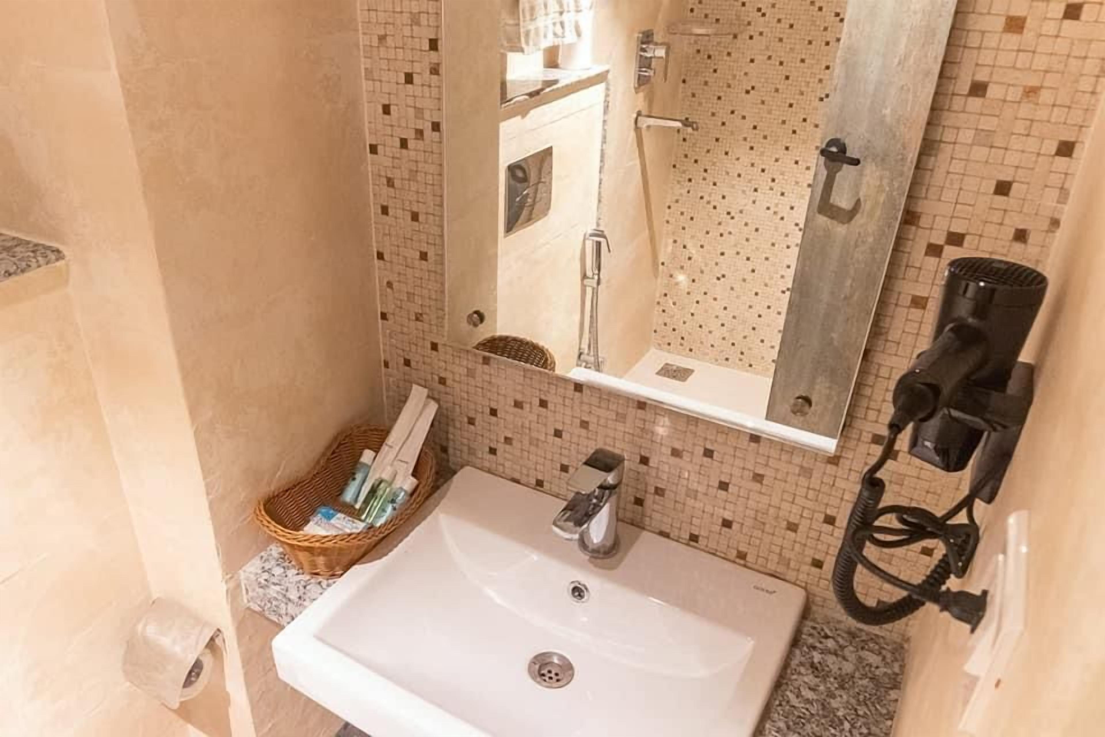 Un baño con lavamanos blanco, un espejo, un perchero para toallas y un secador de pelo.