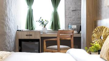 Un dormitorio con un escritorio de madera, una silla, una cama, una planta en maceta y un ventilador de pared.