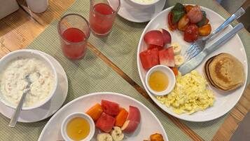 Un desayuno con platos de comida, entre ellos huevos, tortitas y fruta.