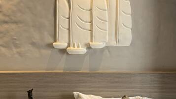A hotel room with a bed, pillows, a vase, and a wall-mounted decorative piece.
