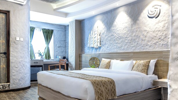 A modern hotel room with a large bed, wooden flooring, a desk with a chair, and a view of the outdoors through a window. - Vastu Boutique Hotel (Kathmandu)