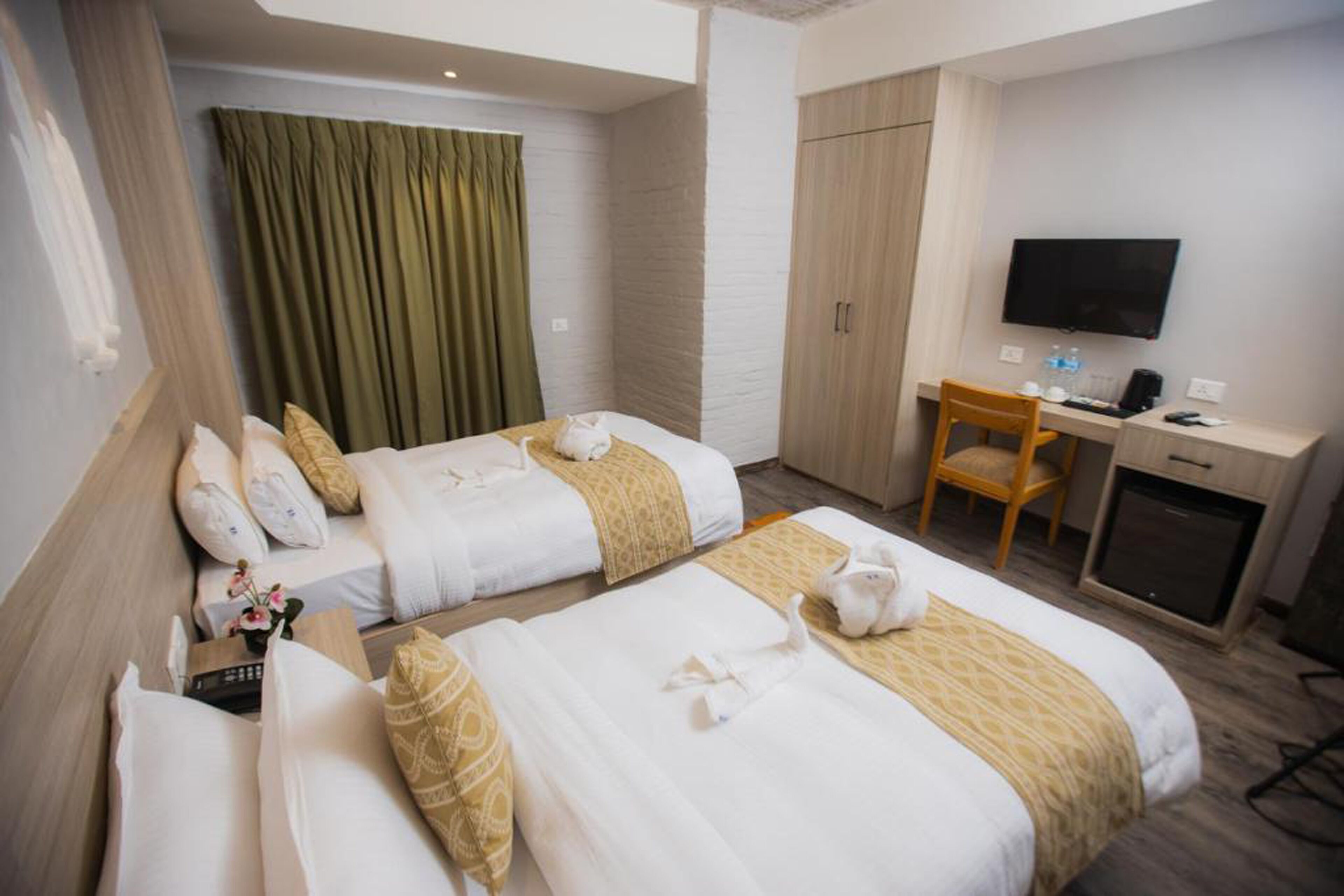 A hotel room with two beds, a desk, a chair, a television, and a wardrobe.