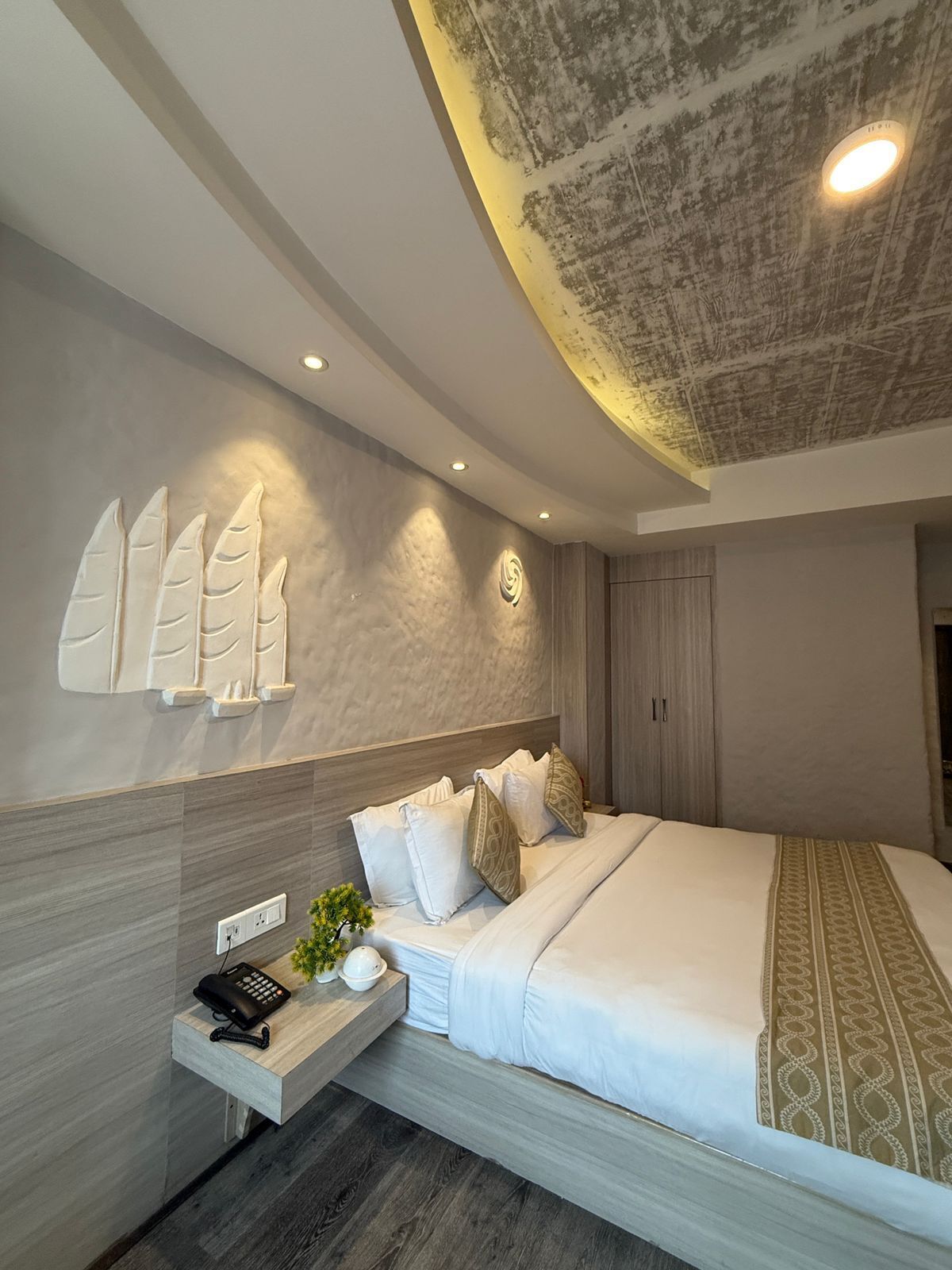Un dormitorio moderno con una cama grande, una mesita de noche con un teléfono y una planta, y un techo con diseño texturizado.