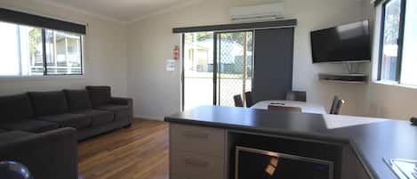 A modern kitchen with a built-in microwave, a dining area with a table and chairs, a gray sofa, and a TV mounted on the wall.