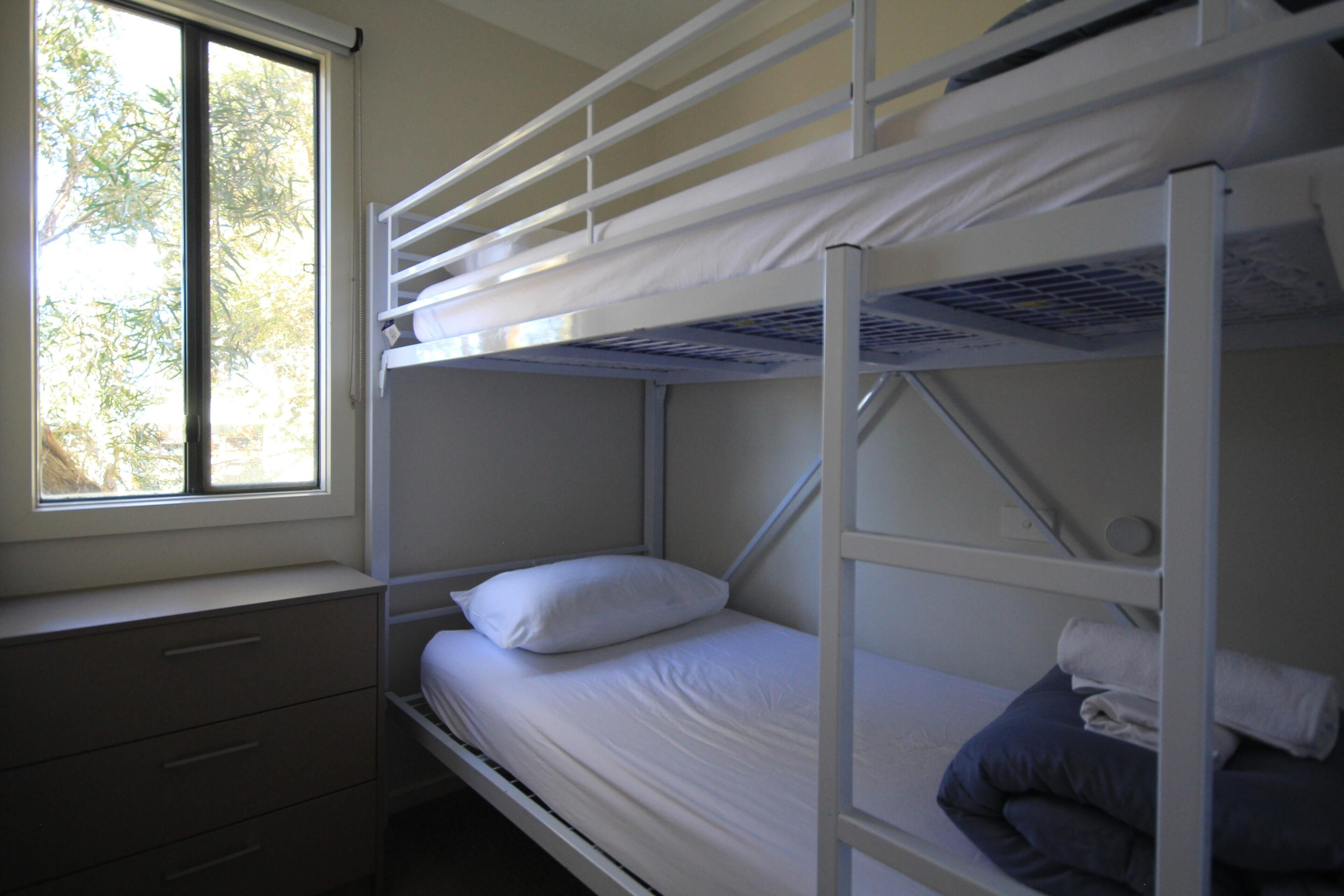 A bunk bed room with a window, a dresser, and a view of trees.