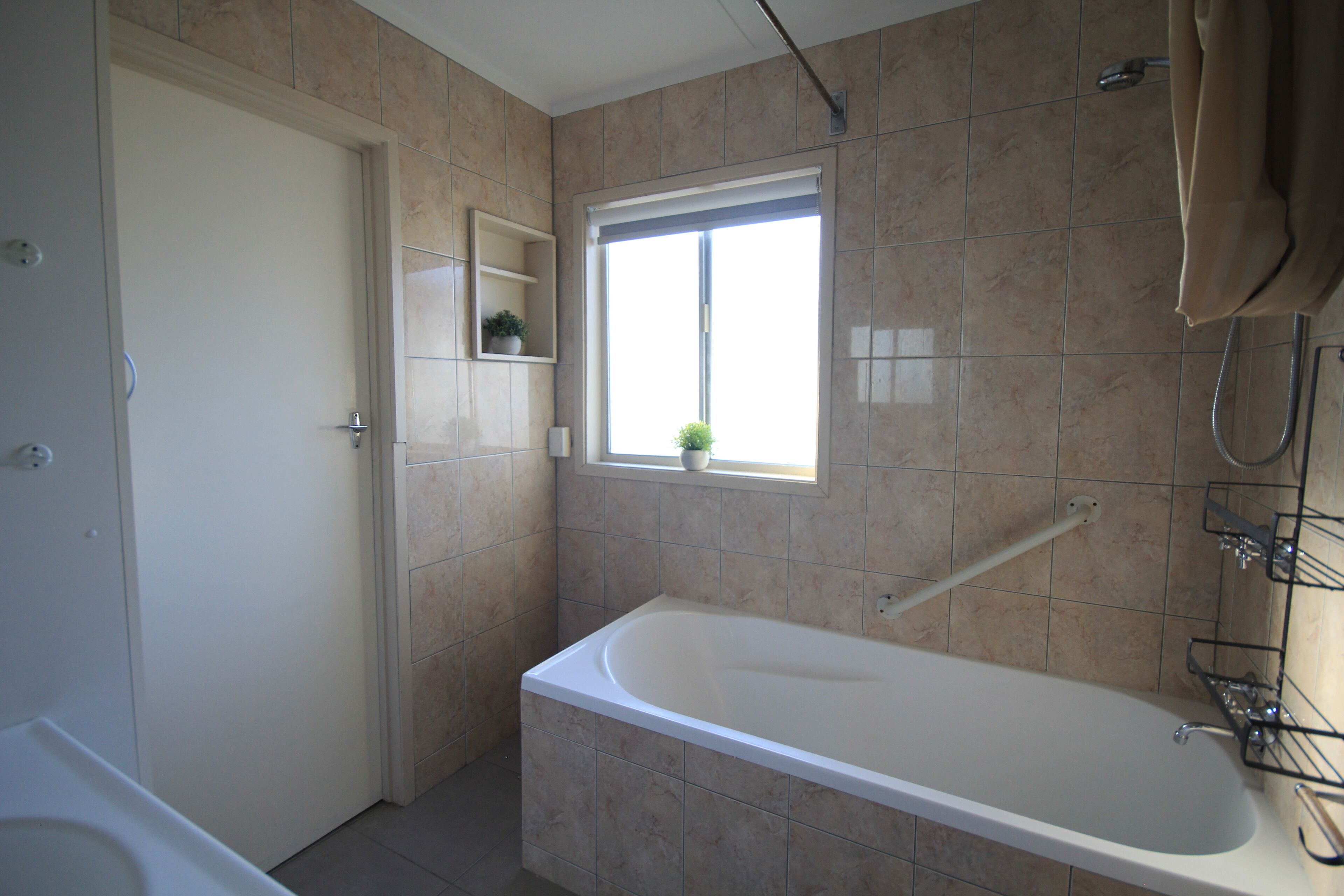 A modern bathroom with a bathtub, a shower, and a window providing natural light.