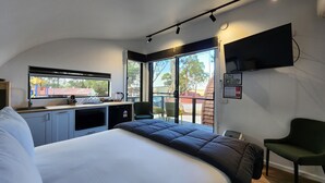 Een moderne hotelkamer met een groot bed, een kitchenette, een aan de muur bevestigde televisie en een balkon met uitzicht.