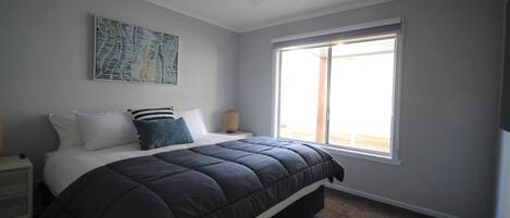 A bedroom with a large bed, a ceiling fan, a window, and a wall-mounted artwork.