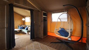 Een gezellige kamer met een hangstoel, een bank met kussens en een houten vloer.