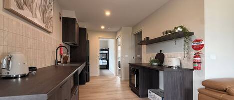 Cozinha moderna com ilha central, armários escuros e vista para o quarto adjacente.