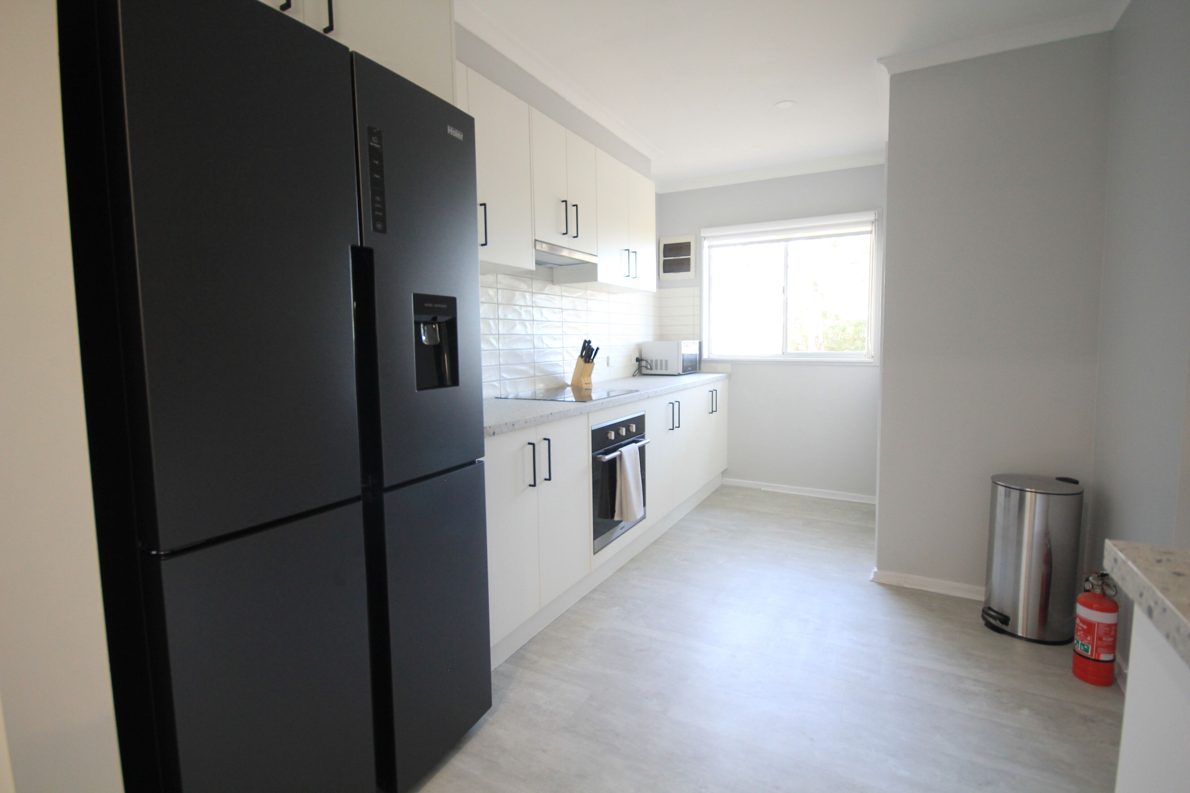 Una cocina moderna con armarios blancos, un refrigerador negro, electrodomésticos de acero inoxidable y un ventanal que proporciona luz natural.
