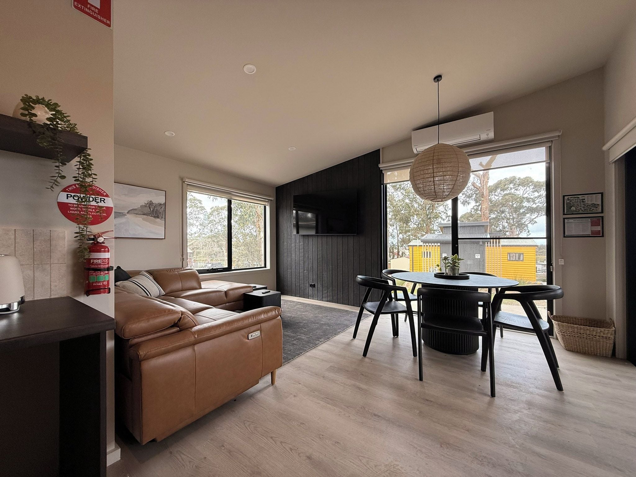 A modern living room with a sofa, a dining table with chairs, and a flat-screen TV mounted on the wall.