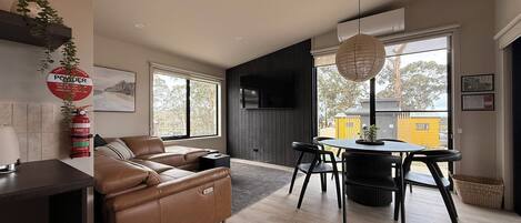 Una sala de estar moderna con un sofá, una mesa de comedor con sillas y un televisor de pantalla plana montado en la pared.