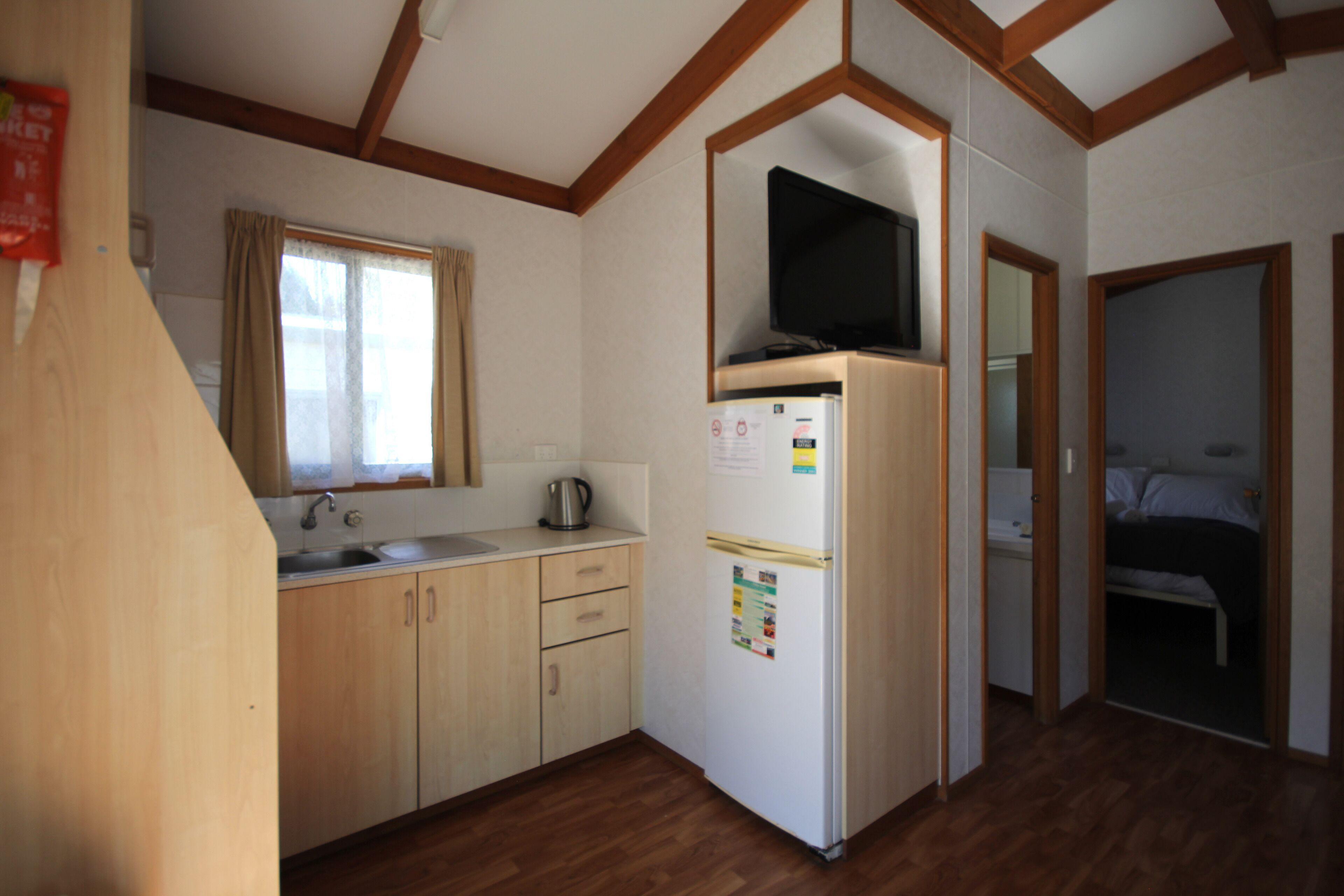 A compact kitchen with wooden cabinets, a refrigerator, and a window with curtains.