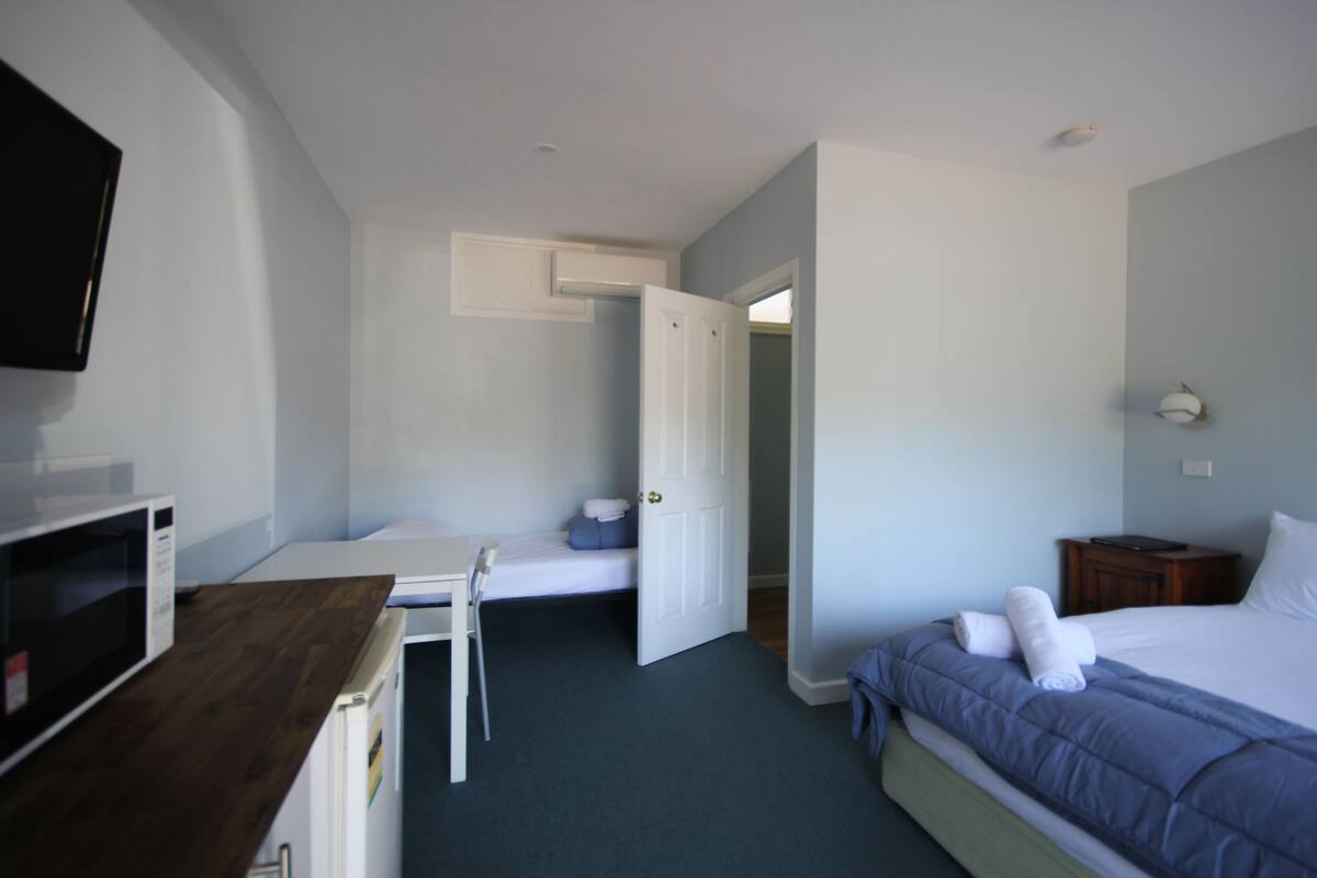 Una habitación de hotel con cama, escritorio con silla, microondas y televisión.