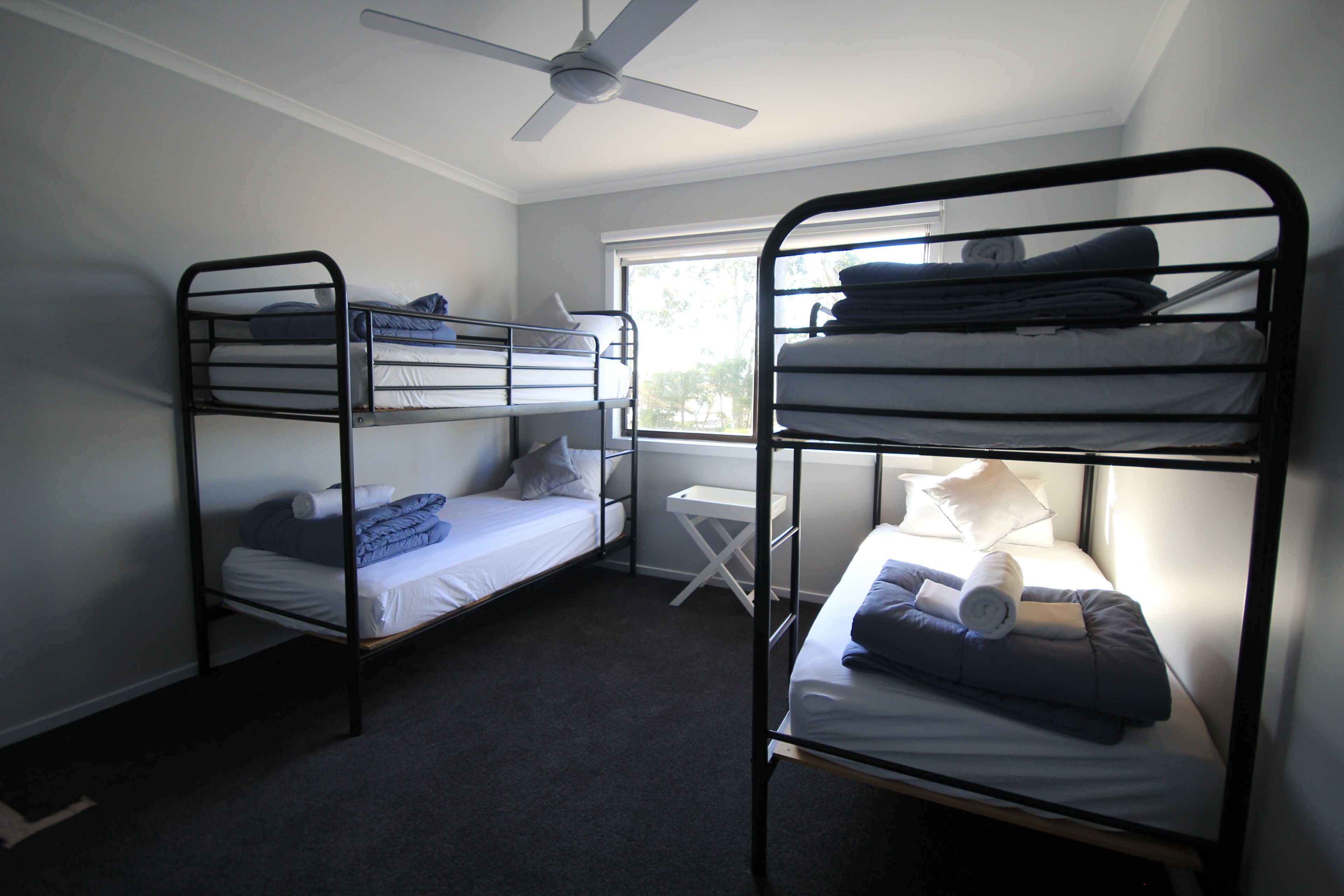 A dormitory room with bunk beds, a ceiling fan, a window, and a small desk.
