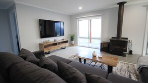 Een moderne woonkamer met een bank, een houten salontafel, een flatscreen televisie, een open haard en een schuifdeur naar een balkon.