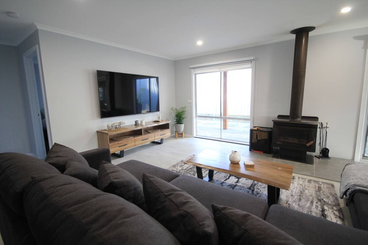 Una sala de estar moderna con un sofá, una mesa de centro de madera, un televisor de pantalla plana, una chimenea y un ventanal corredizo que da a un balcón.
