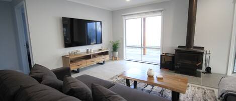 Een moderne woonkamer met een bank, een houten salontafel, een flatscreen televisie, een open haard en een schuifdeur naar een balkon.