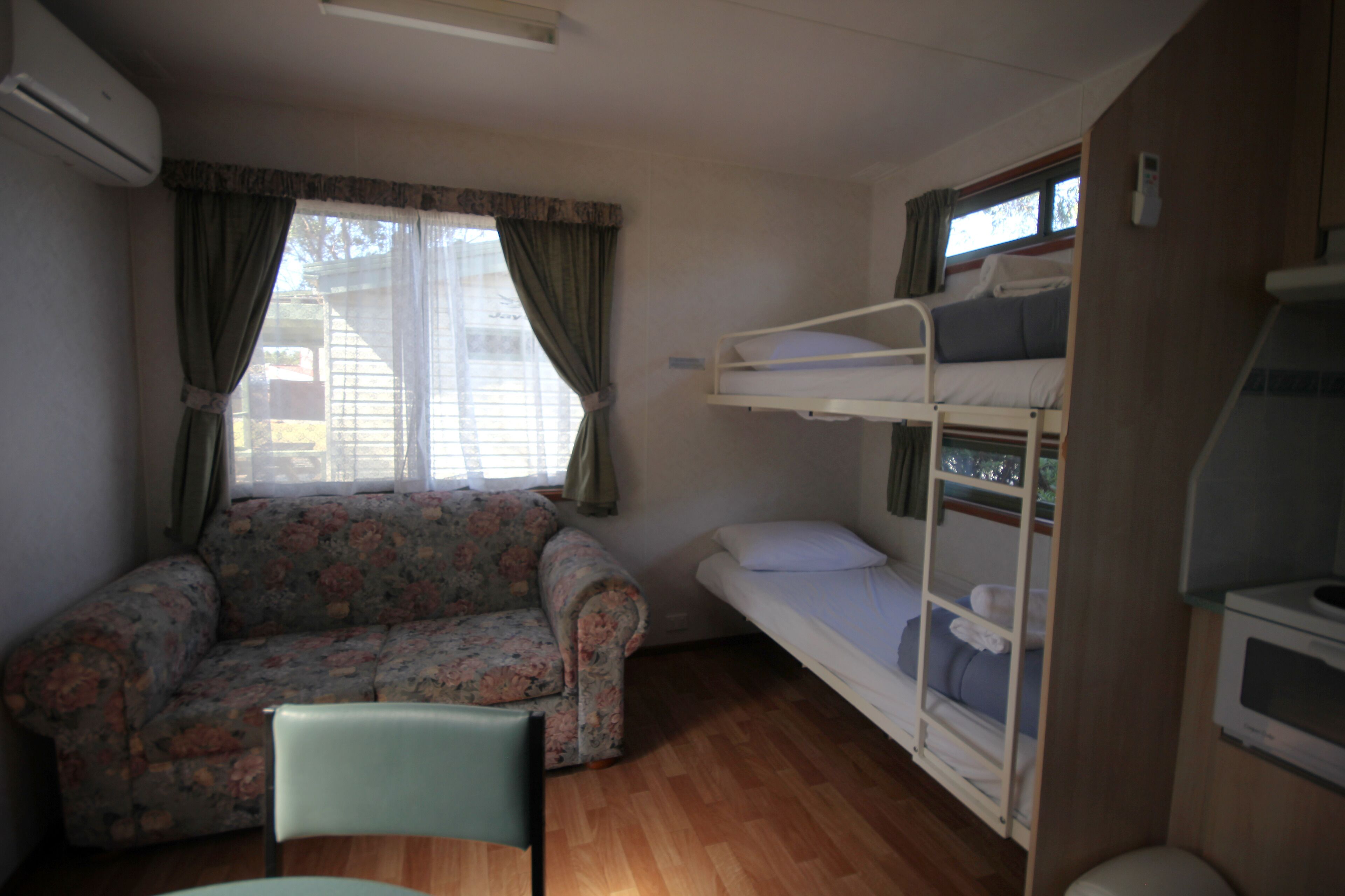 Quarto pequeno e compacto com uma cama de solteiro, um sofá floral e uma única cadeira.