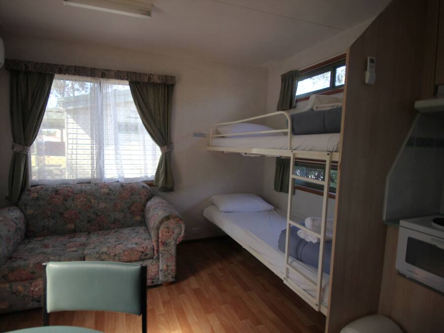 Quarto pequeno e compacto com uma cama de solteiro, um sofá floral e uma única cadeira.