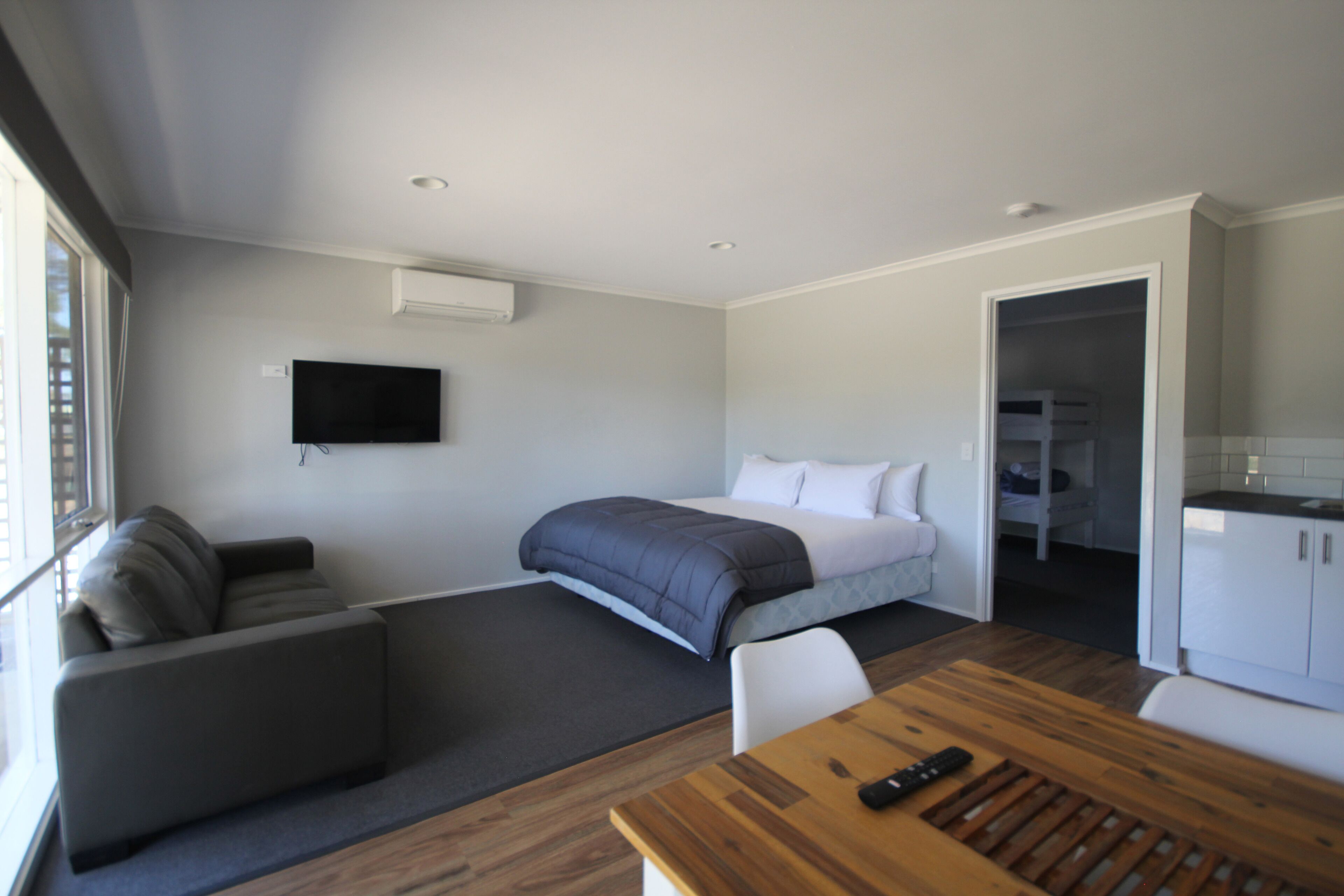 A modern hotel room with a bed, a sofa, a dining table, and a TV.